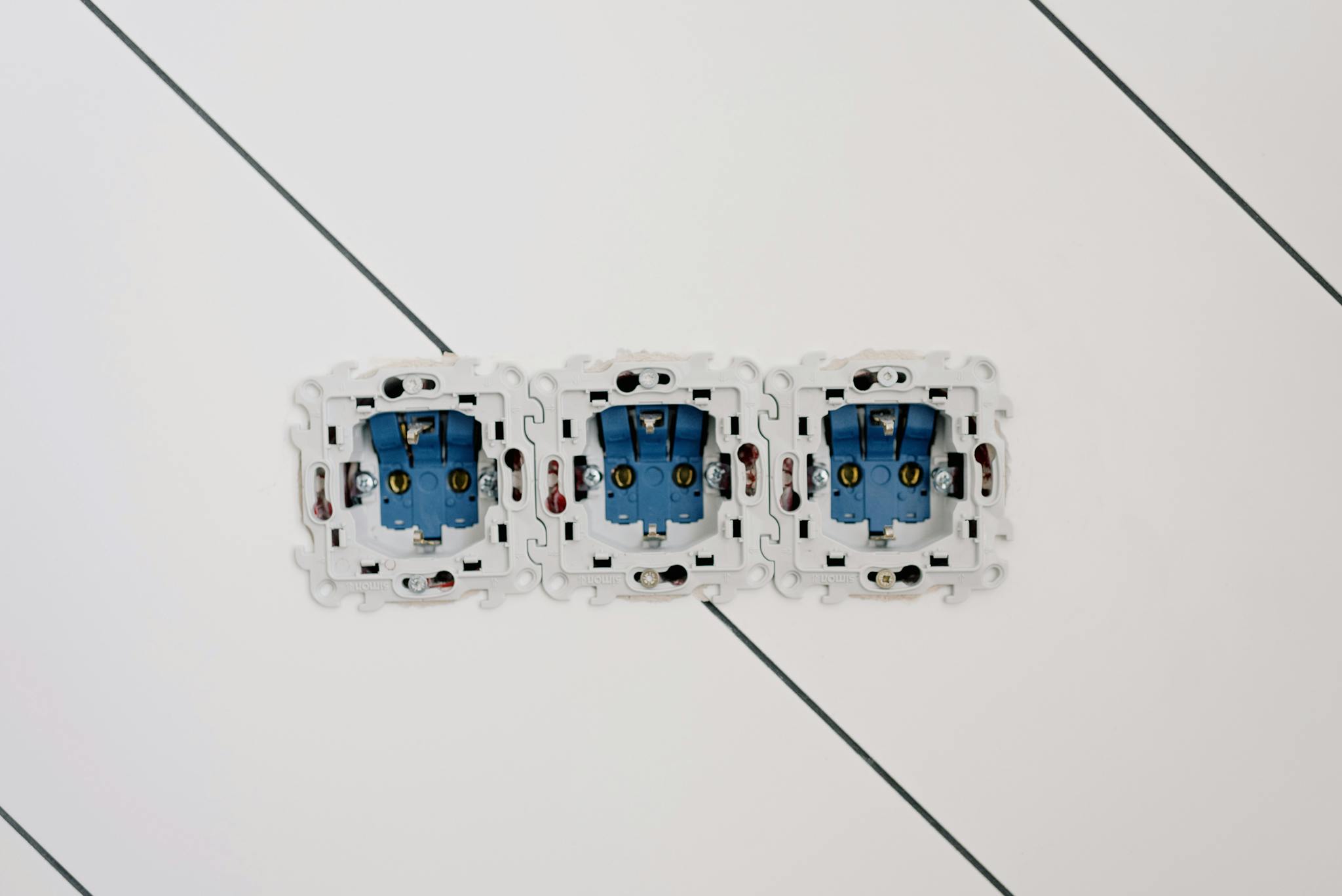 Close-up view of three blue electrical sockets installed in a white wall, showing details of wiring and connections.