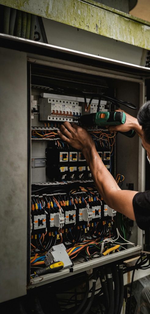 Technician working on circuit breaker panel, adjusting electrical wires indoors.